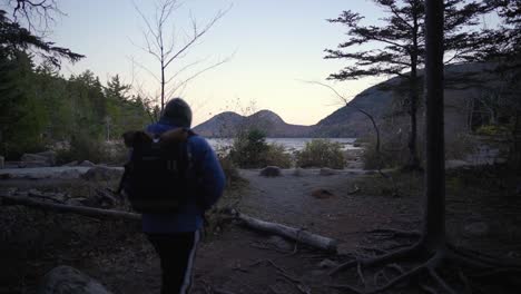Young-man-finishes-a-hike-near-a-lake-at-sunrise-carrying-a-backpack-in-the-winter