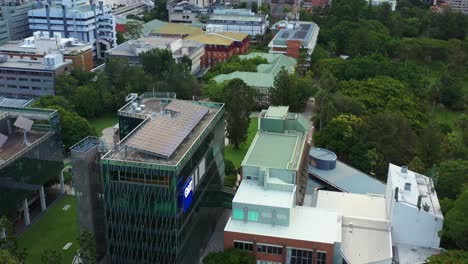 Cinematic-aerial-birds-eye-view-drone-flyover-Queensland-University-of-Technology-research-institution-QUT-gardens-point-campus,-tilt-up-reveals-south-bank-parklands-across-the-river,-Brisbane-city