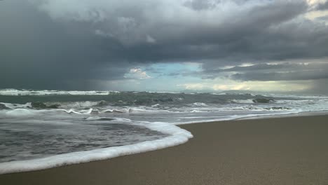 Meereswellen-Laufen-Am-Sandigen-Ufer-Entlang,-Gewitterwolken-Im-Hintergrund