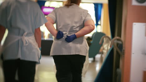 NHS-Nurse-ties-apron-whilst-walking-through-corridor