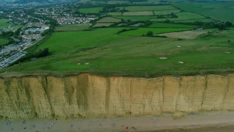 Bridport-West-bay-cliffs-British-countryside-golf-course-aerial-pull-back-reveal-above-turquoise-ocean-coastline