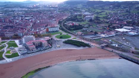 Aerial-view-of-gijon-city-in-north-Spain,-commercial-city-center-with-port-Sandy-beach-and-residential-aerial,-smoky-factory-in-the-background-pollution-gas-emissions