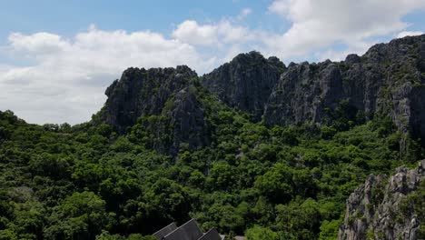 A-closer-descending-footage-of-this-lovely-Buddhist-temple-revealing-limestone-mountains,-and-the-blue-cloudy-sky