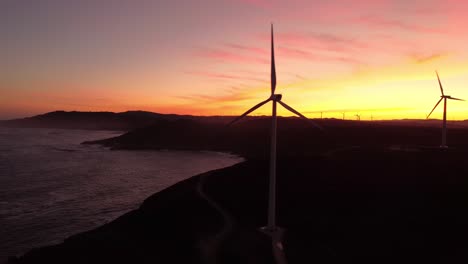 Aerial-view-of-windmill-wind-turbines-farm-silhouette-with-sunset-colourful-sky-and-ocean-cliff-natural-seascape