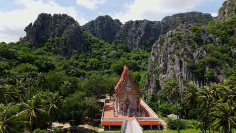 Reverse-aerial-footage-of-his-famous-Buddhist-temple-in-the-forest-surrounded-by-limestone-mountains-and-coconut-trees