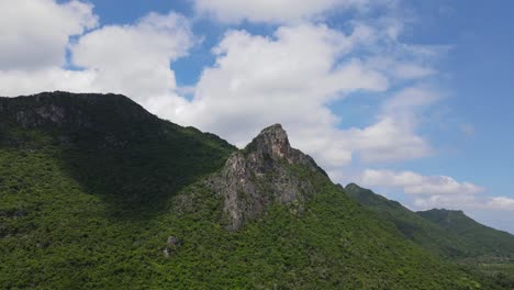 A-steady-aerial-footage-of-this-mountain-covered-with-trees-and-a-rock-tower-jutting-out-with-beautiful-blue-sky-and-clouds-moving,-Sam-Roi-Yot-National-Park,-Prachuap-Khiri-Khan,-Thailand
