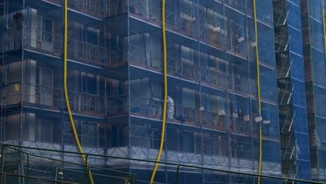 Close-up-View-of-a-construction-site-where-workers-are-working-in-asbestos-suits-within-blue-safety-net