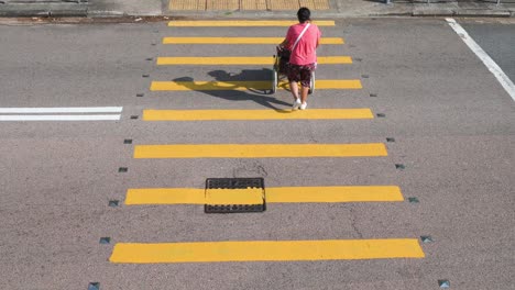 Junge-Frau,-Die-Einen-älteren-Mann-In-Einem-Rollstuhl-Schiebt,-Während-Sie-Durch-Einen-Zebrastreifen-Gehen,-Während-Ein-Männlicher-Fußgänger-Hinter-Ihnen-Ebenfalls-In-Hongkong-Hinübergeht