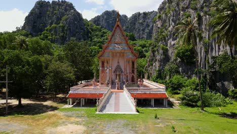 A-steady-aerial-footage-of-this-Buddhist-temple-within-the-limestone-mountains,-forest,-coconut-trees