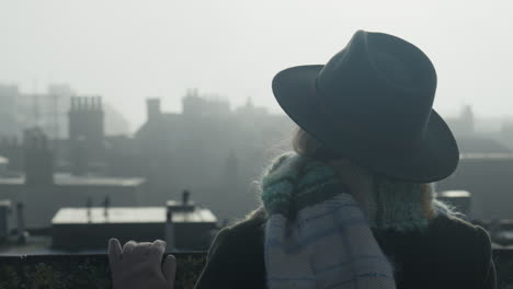 Woman-in-hat-watching-medieval-city-rooftops-in-misty-morning