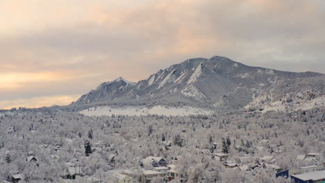 Low-drone-shot-moving-down-of-Boulder-Colorado-and-rocky-Flatiron-mountains-after-large-winter-snow-storm-covers-trees,-homes,-streets,-and-neighborhood-in-fresh-white-snow