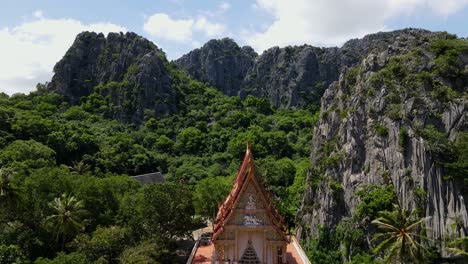 Ascending-aerial-footage-of-the-Wat-Khao-Daeng-with-limestone-mountains-and-a-forest-in-Khao-Sam-Roi-Yot-National-Park,-Phrachuap-Khiri-Khan,-Thailand