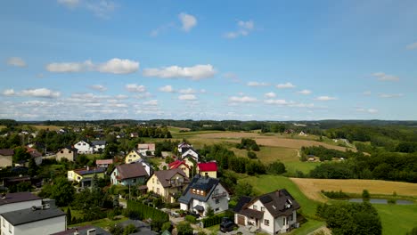 Cottage-houses-on-beautiful-green-meadows-surrounded-by-green-forest-in-Brodnica---aerial-descending