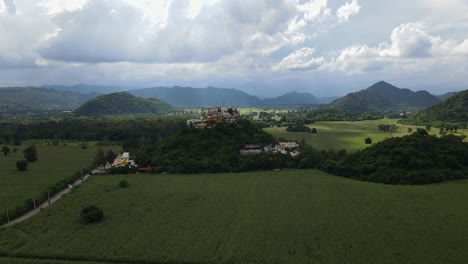 Descending-aerial-footage-revealing-this-corn-fields-and-the-famous-Simalai-Songtham-Temple-with-amazing-background-in-Khao-Yai,-Pak-Chong,-Thailand