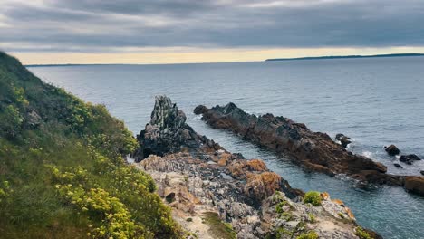Slow-motion-shot-of-a-guy-climbing-rocks-of-Bretagne-by-the-side-of-a-pleasant-calm-ocean-water-waves-in-the-summer