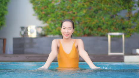 Childish-Asian-Woman-in-Swimming-Pool-Spraying-Water-and-Looking-at-Camera,-Full-Frame