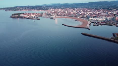 Panoramic-aerial-drone-footage-of-gijon-cityscape-at-sunset,-beach-port-commercial-touristic-harbor,-north-of-Spain