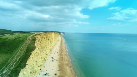 Bridport-West-bay-aerial-view-close-to-cliffs-above-British-seaside-turquoise-ocean-coastline,-Dorset