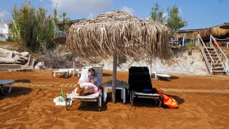 A-Female-Tourist-Lying-Relaxed-On-A-Sunbed-With-Reed-Canopy-In-Megas-Lakkos-Beach,-Kefalonia,-Greece---static-shot