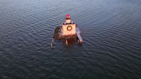 An-aerial-view-of-the-Huntington-Harbor-Lighthouse-on-Long-Island,-NY-at-sunset,-with-a-Christmas-wreath-on-it