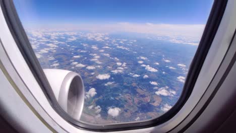 Blick-Aus-Einem-Flugzeugfenster-Auf-Wolken-Und-Den-Boden,-Sonniger-Tag
