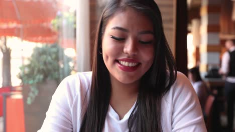 Attractive-cute-girl-in-a-cafe-during-a-date-marvels-and-smiles-at-the-camera-while-blushing