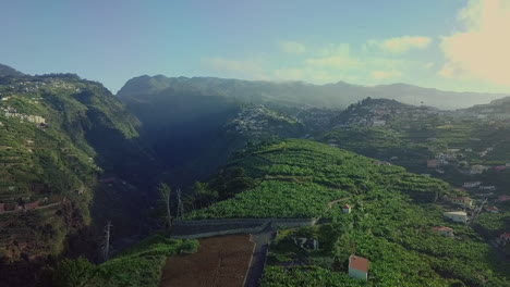 Aerial-view-over-hillside-farms-with-scenic-mountains-in-distance,-Madeira-PT