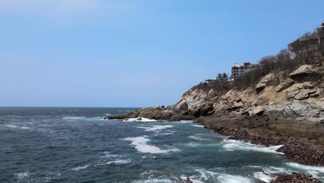 Pull-front-above-rocks-and-waves-with-view-of-cliff-and-small-hotel-in-Oaxaca,-Mexico