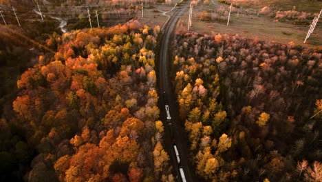 Freight-Train-Travels-through-a-Vibrant-Fall-Corridor-next-to-a-River,-Vibrant-Autumn-Aerial-View,-Canada