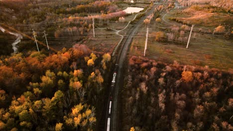 Slow-Camera-Tilt-tracking-a-Freight-Train-travelling-through-an-Vibrant-Fall-Autumn-Landscape,-Aerial-View,-Canada