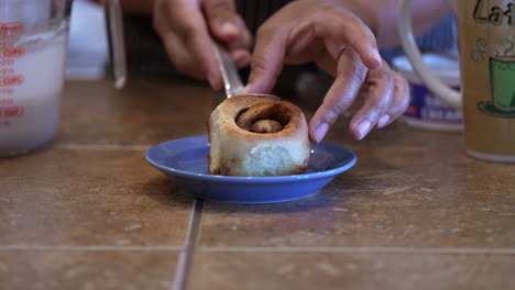 Placing-a-fresh-baked-cinnamon-roll-on-a-plate-for-icing-and-serving---side-view-in-slow-motion