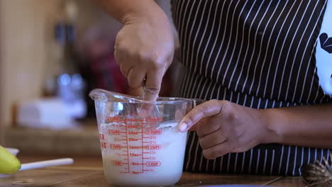 Stirring-icing-in-a-measuring-cup-with-a-metal-whisk---side-view-in-slow-motion