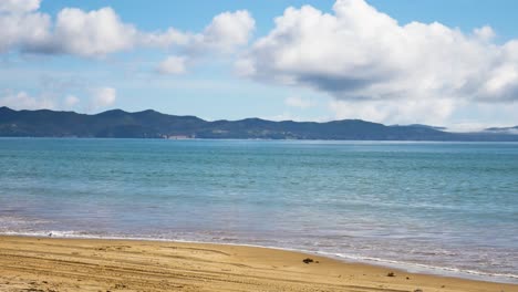Tropical-Maitai-Bay-with-reaching-water-on-sandy-beach-during-sunny-day-and-cloudy-day-in-New-Zealand---No-people-at-shore---Panning-shot