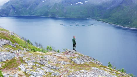 Excursionista-Masculino-De-Pie-En-La-Zona-De-Senderismo-Cerca-Del-Pico-De-La-Montaña-Segla-Con-Vistas-Al-Fiordo-En-Senja,-Noruega
