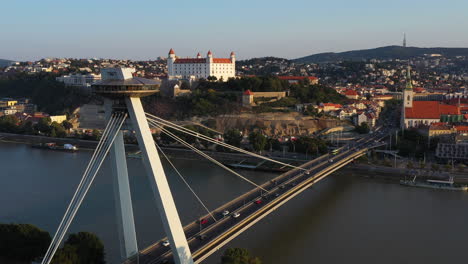 Cinematic-drone-shot-of-the-Bridge-of-the-Slovak-National-Uprising-and-the-Bratislava-Castle-in-the-background-in-Bratislava,-Slovakia