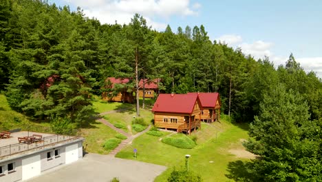Forest-Wooden-Cottages-with-Red-roofs-for-travelers-accommodation-in-Borucino,-Poland---drone-shot