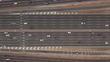 Drone-view-from-above-of-a-large-highway-with-several-lanes-on-which-many-cars-are-driving,-going-about-their-routine