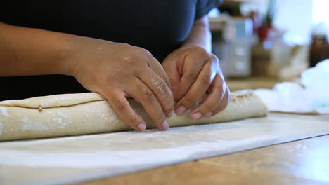 After-rolling-dough,-sugar-and-cinnamon-into-a-roll,-the-chef-pinches-the-seam-together-to-press-and-seal-before-slicing-into-rolls