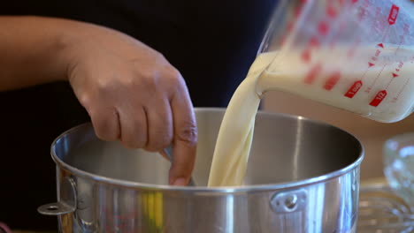 Pouring-milk-into-a-mixing-bowl-to-make-a-tasty-homemade-treat---stirring-in-the-ingredients-in-slow-motion,-side-view