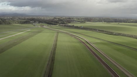 Green-aerial-flyover-of-horse-race-track-under-overcast-Irish-sky