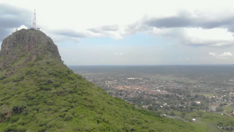 Luftaufnahme,-Die-Sich-über-Eine-Große-Felsklippe-Mit-Einer-Kleinen-Afrikanischen-Stadt-An-Ihrem-Fuß-Vorwärts-Bewegt