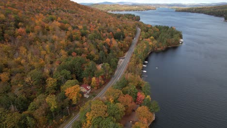 Lake-Sunapee-Coastline-on-Autumn,-Aerial-View-of-Colorful-Foliage,-Cars-on-Road-and-Lakefront-Houses,-Drone-Shot