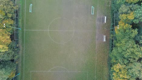 Cinematic-straight-down-aerial-shot-of-football-pitch-hidden-in-green-autumn-forest
