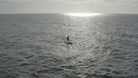 Aerial-retreats-from-SUP-paddle-boarder-in-sun-beam-on-choppy-ocean