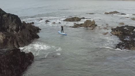 Wetsuit-paddleboarder-on-chaotic-water-around-ocean-islets-at-low-tide