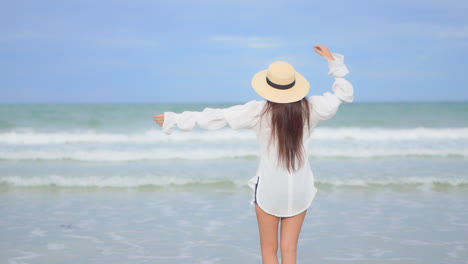 Back-view--Young-girl-standing-seafront-and-raising-arms-up-during-a-morning-walk-on-island's-beach,-sea-waves-with-foam-rolling-over-the-beach-in-Miami,-USA