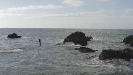 Aerial:-Rough-ocean-water-challenges-stand-up-paddleboarder-near-rocks
