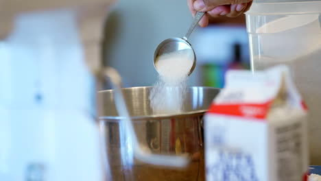 Adding-sugar-to-the-mixing-bowl-for-a-homemade-dessert-made-by-mom---slow-motion