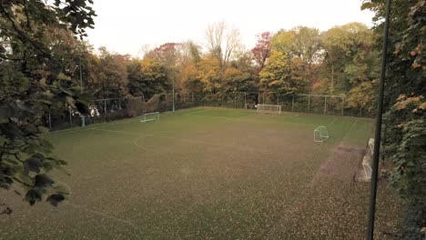 Aerial-tracking-shot-of-the-empty-autumn-soccer-field,-colorful-fallen-leaves-on-the-pitch-playground