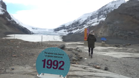 Frau-Zu-Fuß-Durch-Die-Jahresmarke-1992-Des-Athabasca-Gletschers,-Sich-Zurückziehendes-Eisfeld-In-Alberta,-Kanada